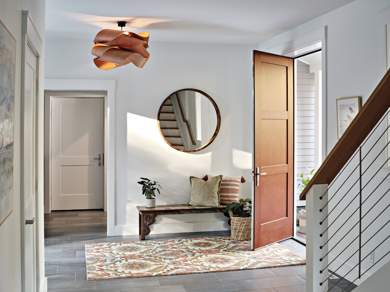 Modern entryway with wooden bench, round mirror, and warm-toned light fixture