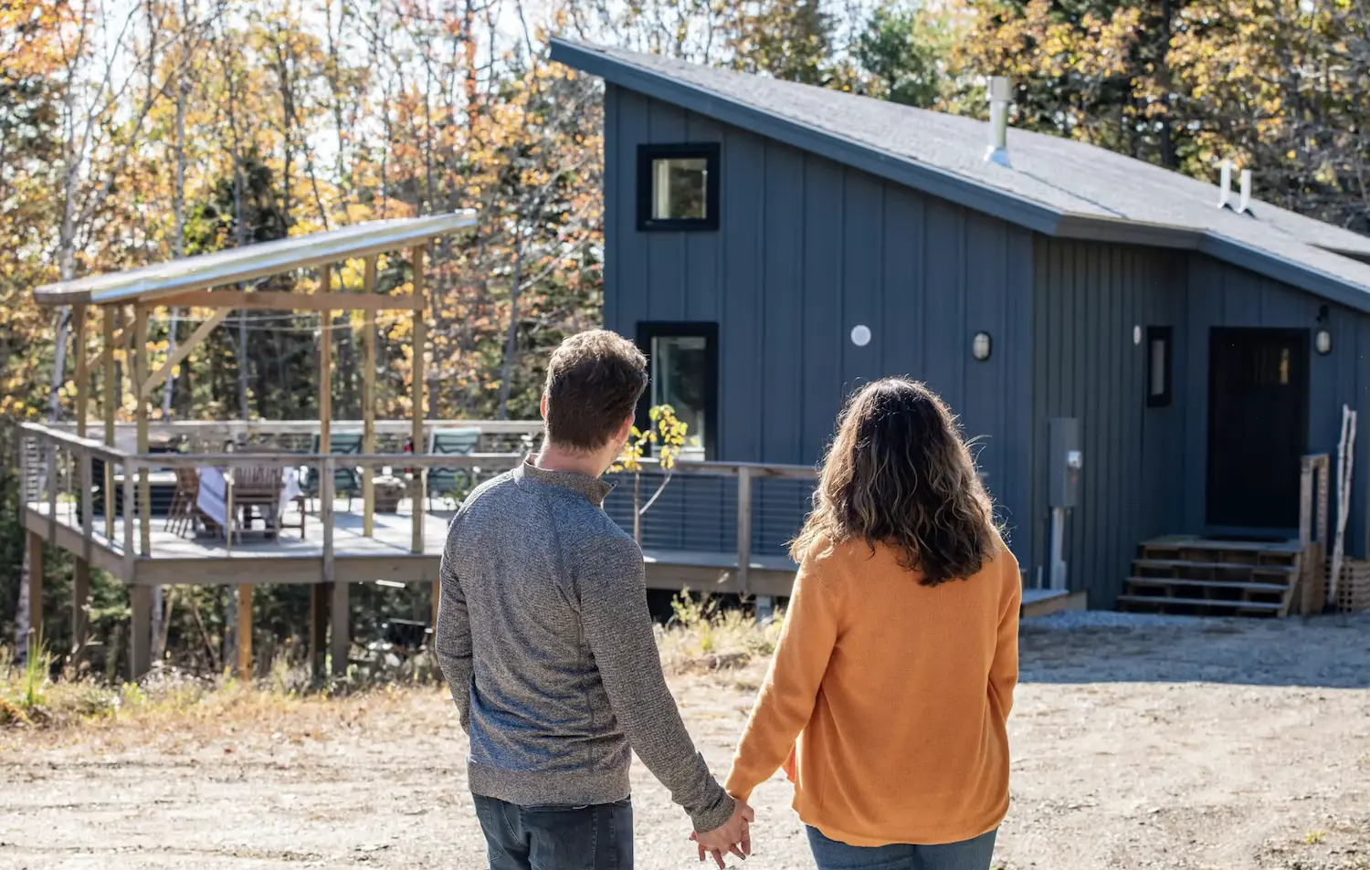 Couple holding hands looking at modern blue cabin in autumn woods