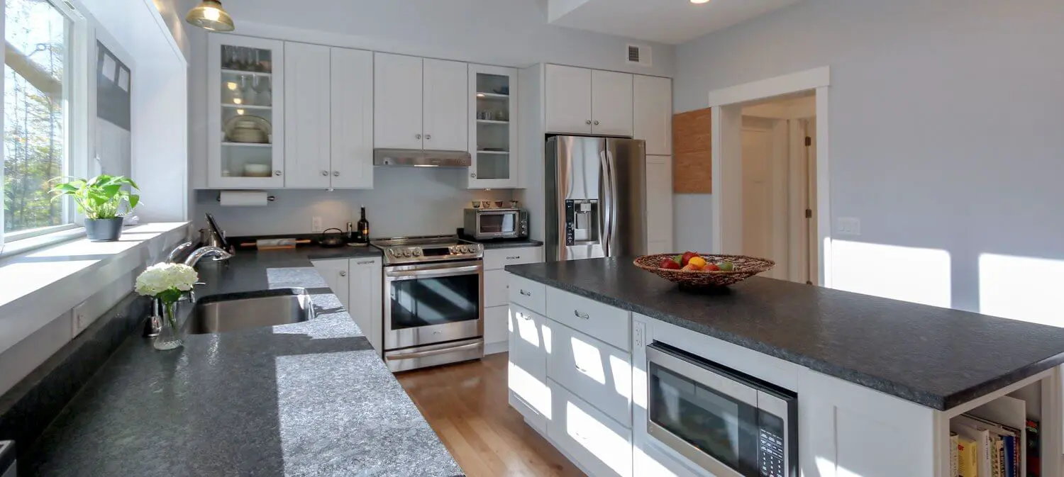 Modern white kitchen with black countertops, stainless steel appliances, and natural light