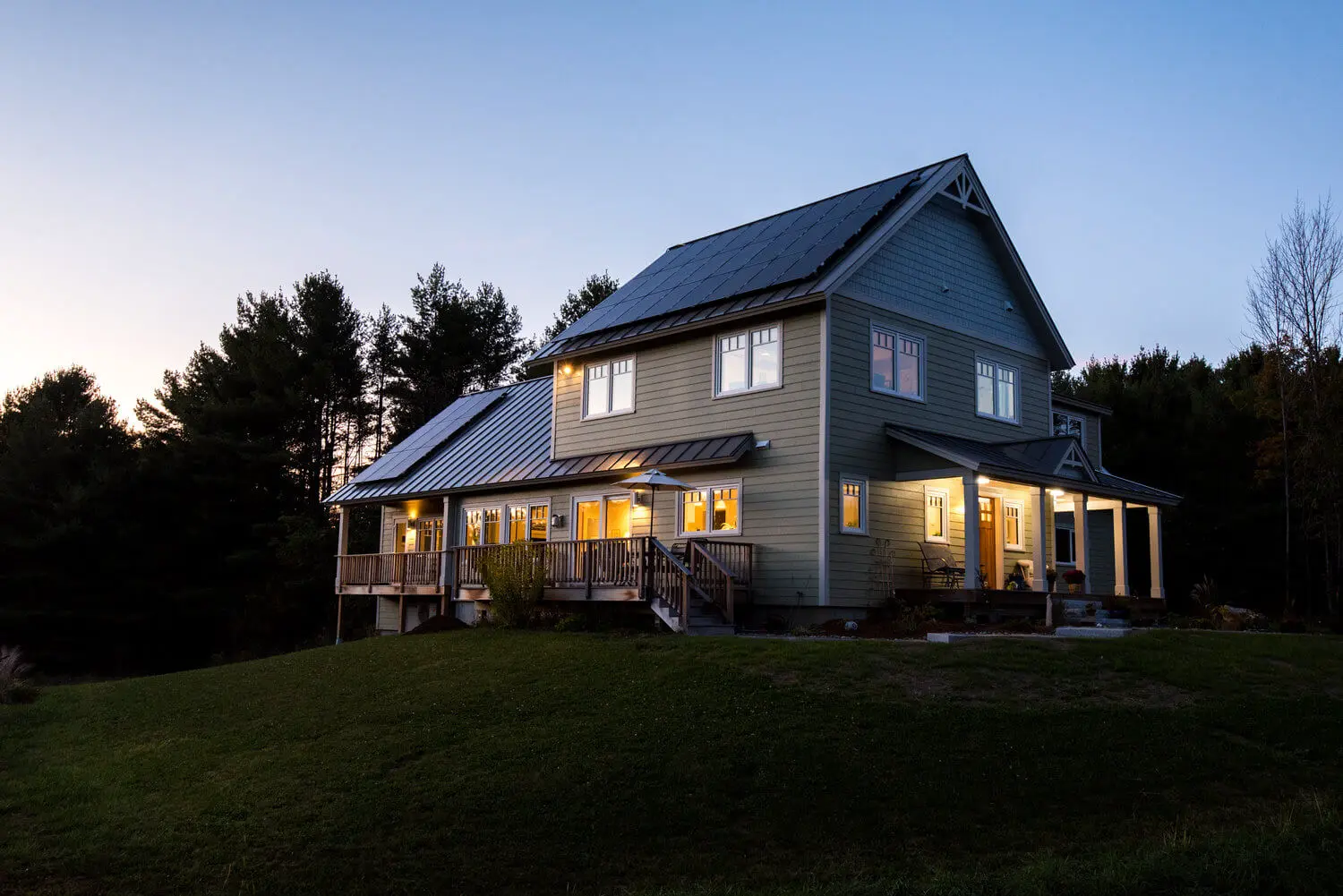 Modern two-story house with solar panels, illuminated at twilight among pine trees