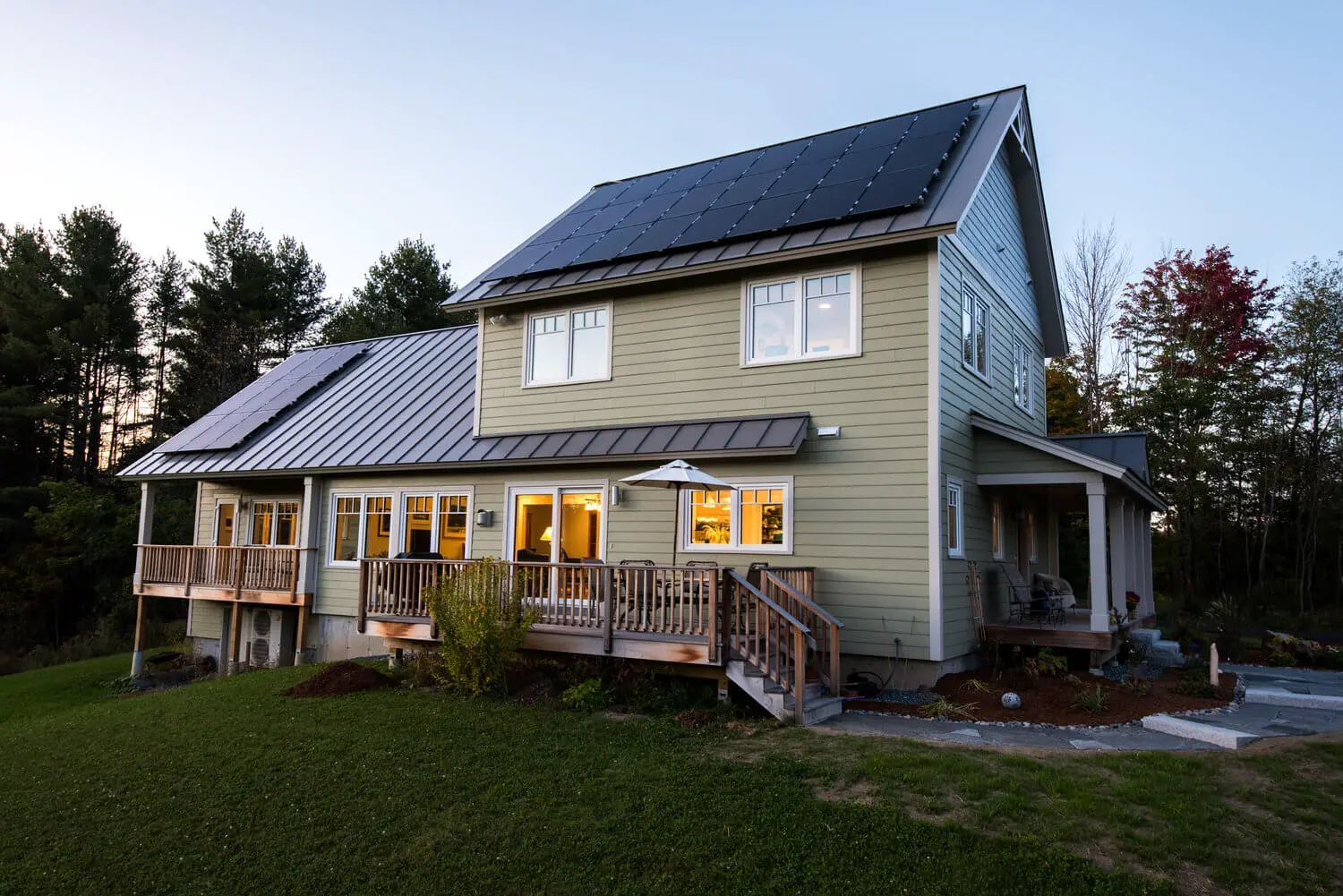Modern two-story house with solar panels, wooden deck, and warm evening lighting