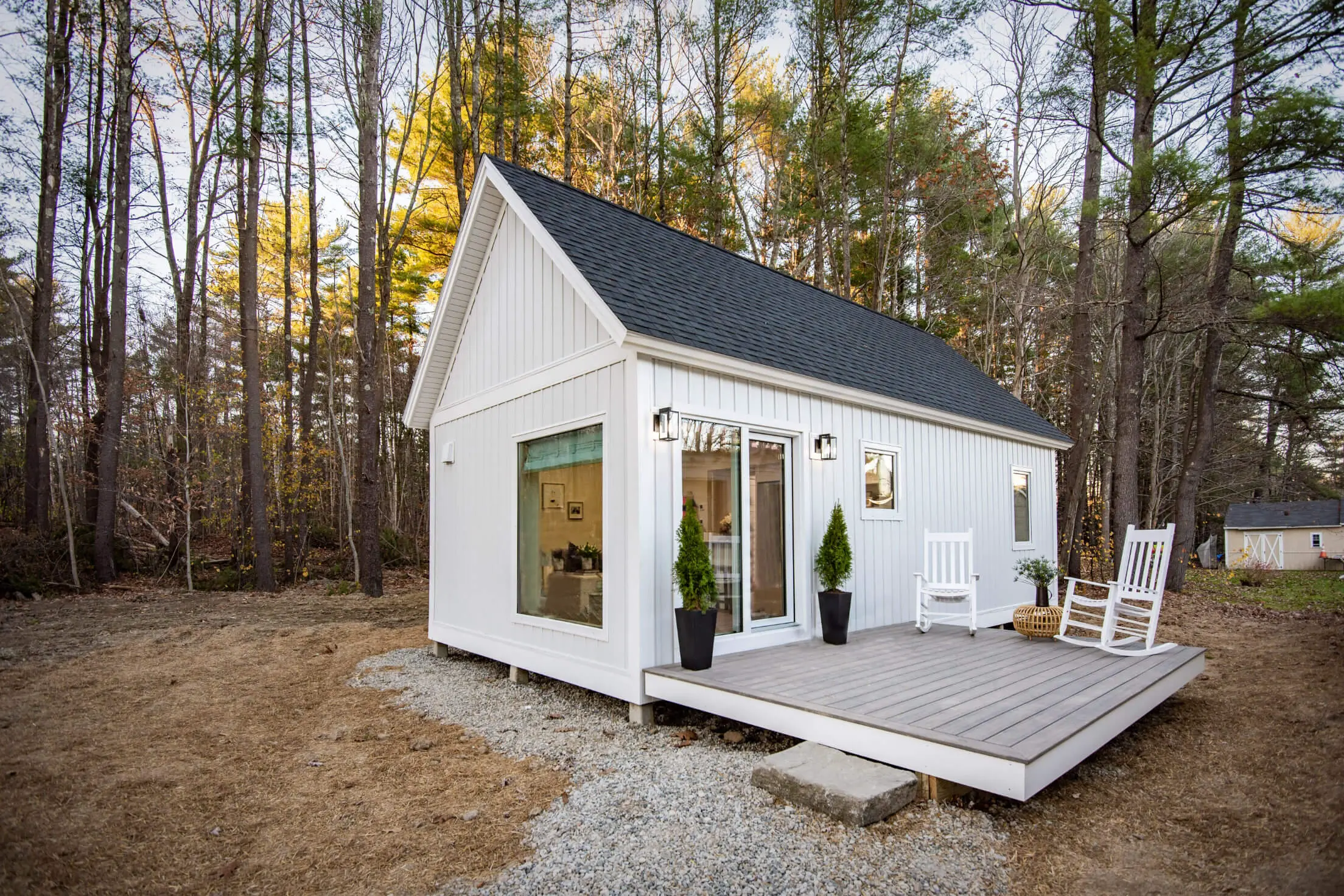 White tiny house with deck nestled in autumn forest surrounded by trees
