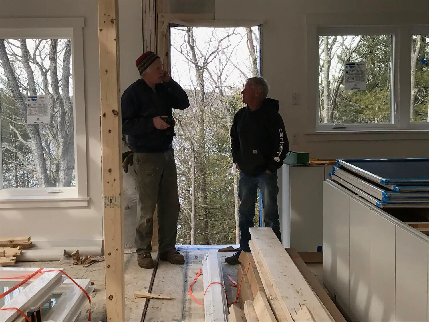 Two workers discussing construction project inside unfinished room with winter trees