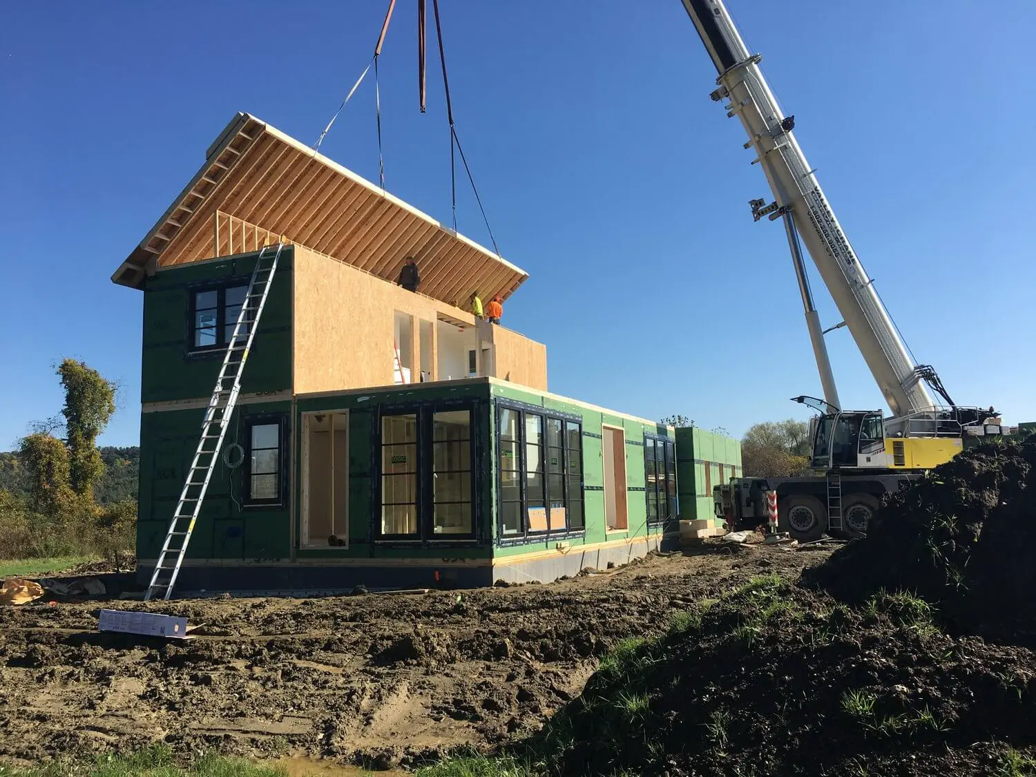 Modular house being lifted by crane during construction on muddy site