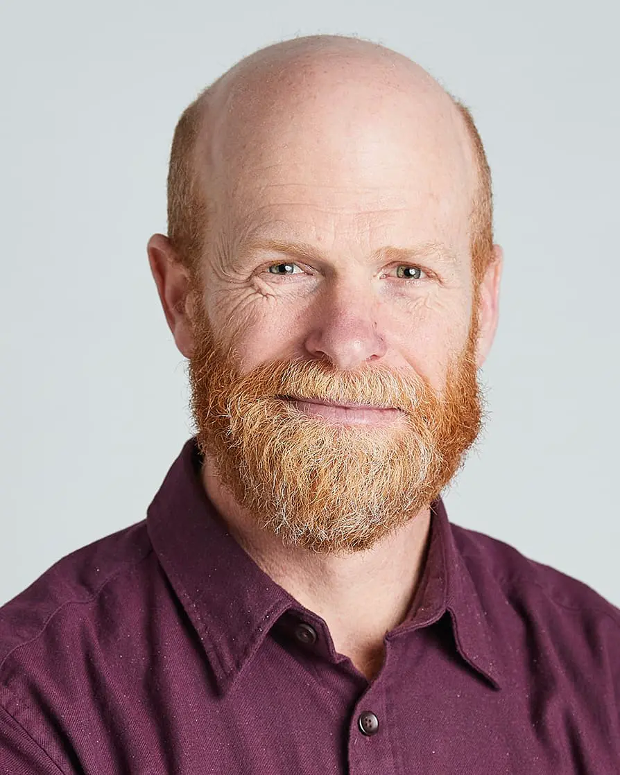 Bald man with vibrant red beard smiling in burgundy shirt