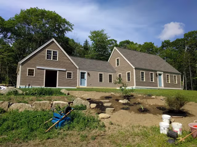 Beige house with blue doors surrounded by trees and landscaping rocks