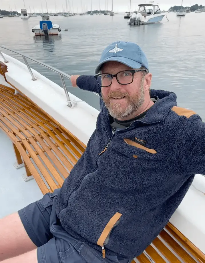 Smiling person in blue fleece jacket sitting on boat at marina