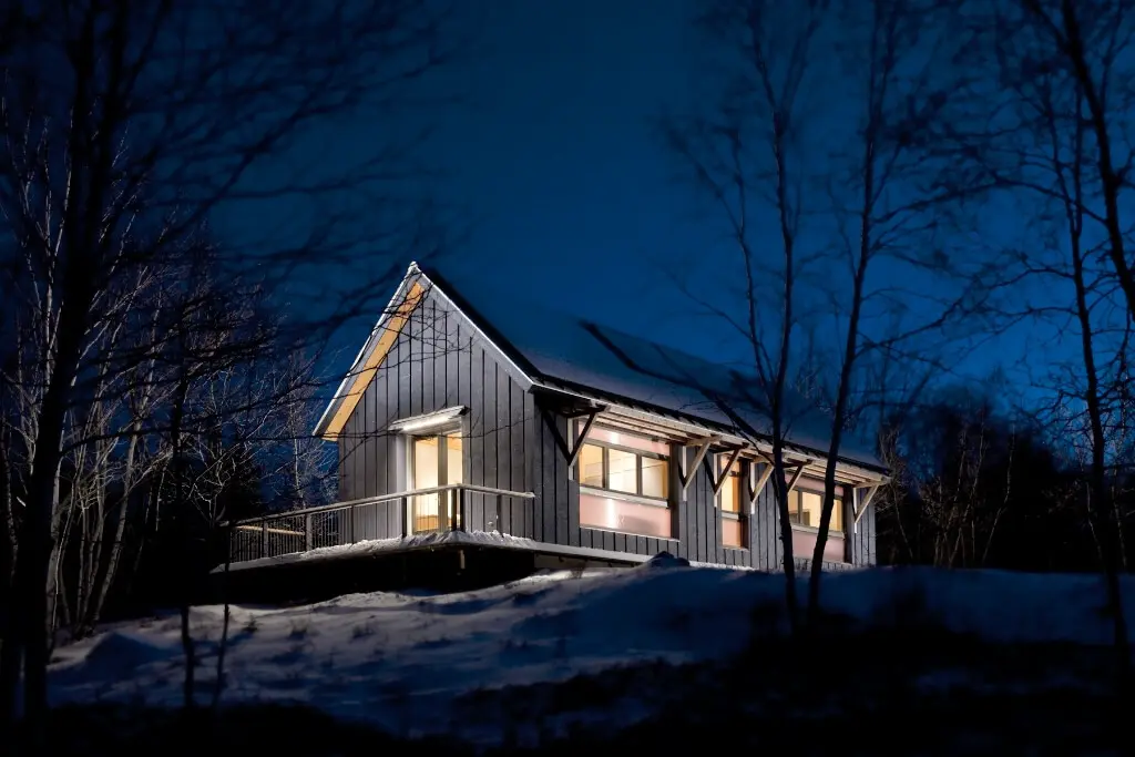 Warm-lit modern cabin nestled in snowy winter woods at night