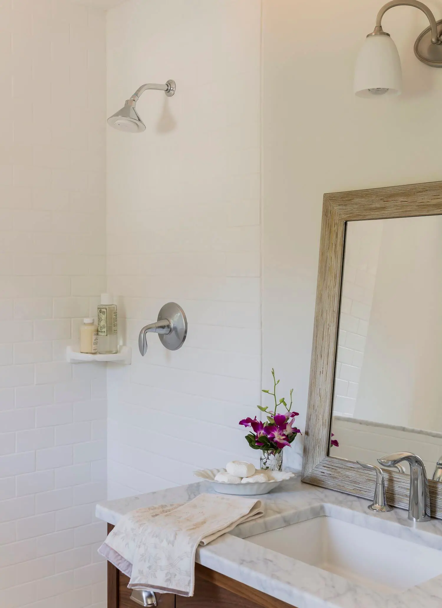 Clean bathroom with white tiles, marble countertop, and purple orchid