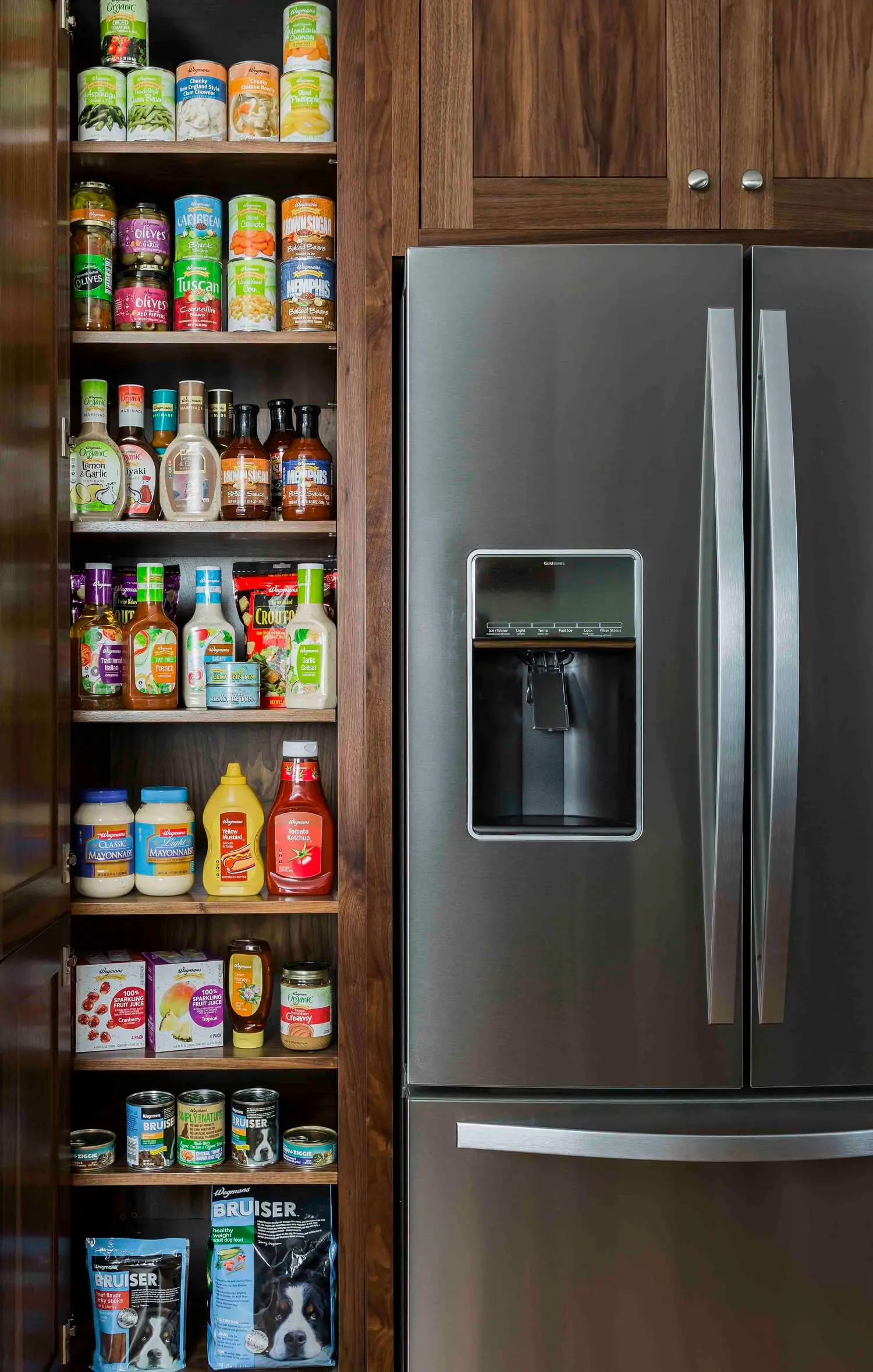 Wooden pantry shelves filled with condiments beside a stainless steel refrigerator