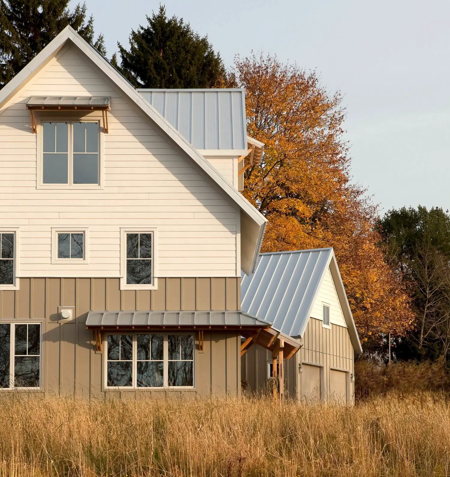 Modern farmhouse with metal roof in golden autumn field landscape