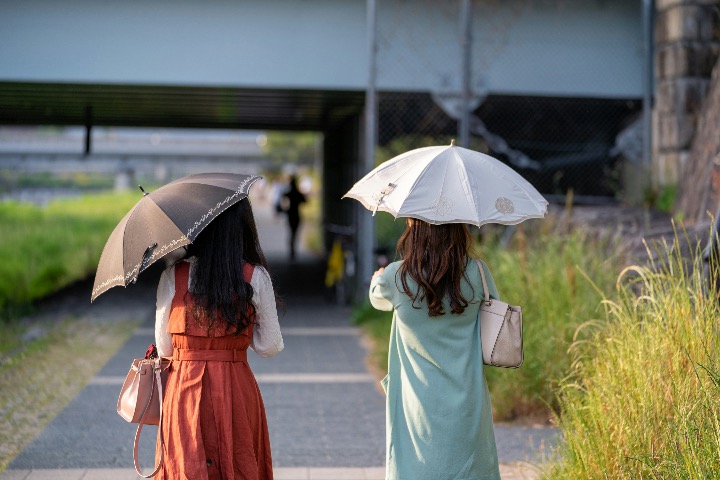 Two women walking with parasols on a sunny path during summer in Japan