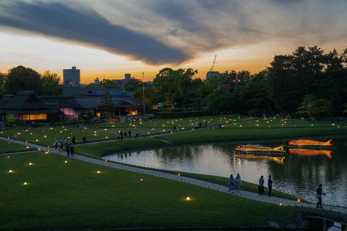 Traditional Japanese garden lit up with lanterns with people strolling at sunset