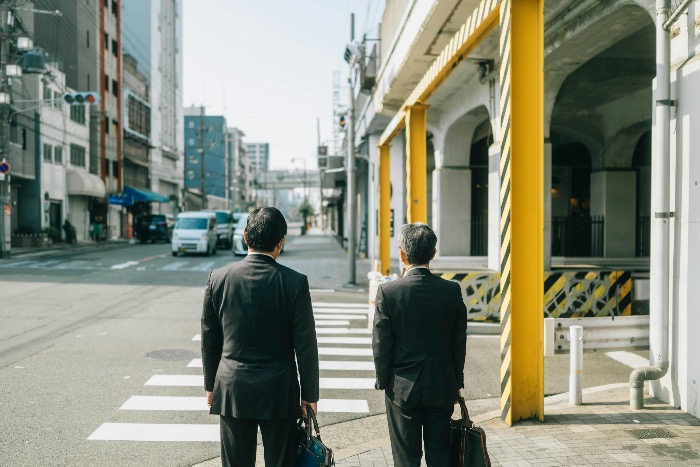 Two men in business suits waiting at a crosswalk in Japan