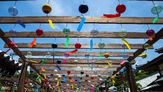 Japanese summer wind chimes (furin) with colorful tags hanging from a wooden pergola