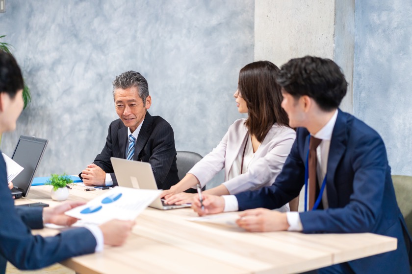 A business meeting in progress with an older man seated at the center and younger colleagues listening attentively.