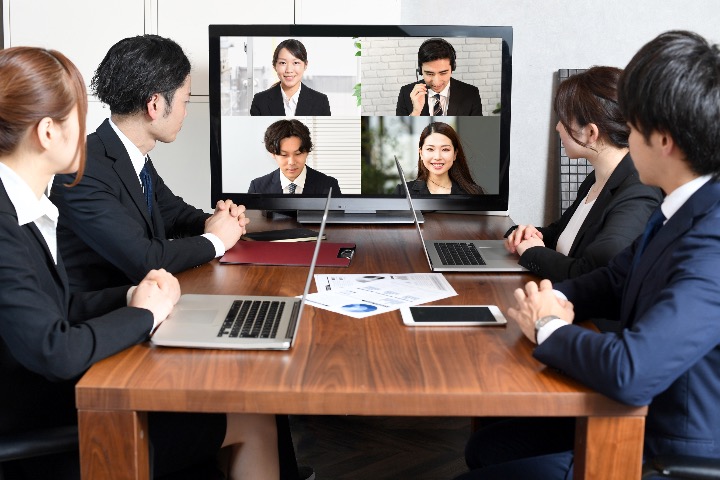 Team members attending a hybrid meeting, some on video call and others in-person, with charts on the table.