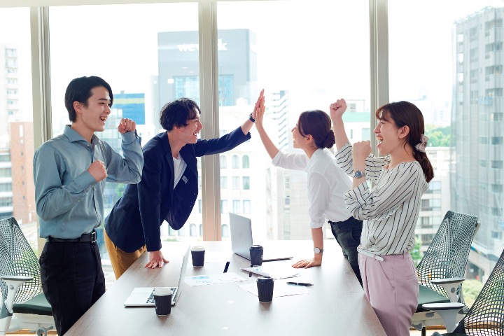 Young professionals in an office celebrating with a high five