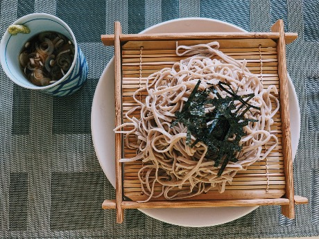 A plate of zaru soba served on a bamboo mat with dipping sauce on the side, topped with shredded nori seaweed.