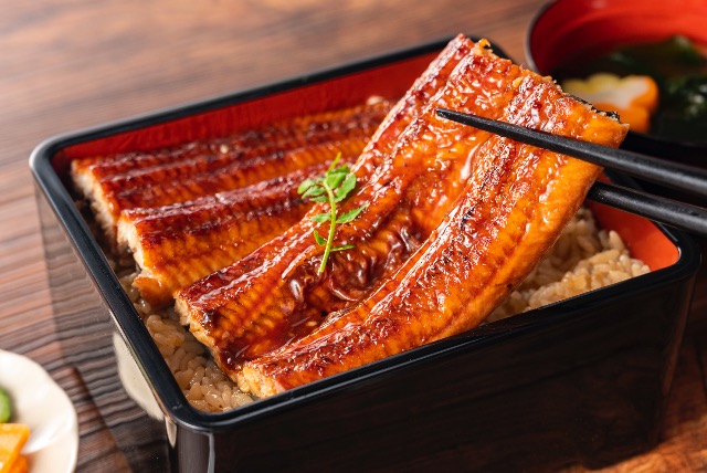 Grilled eel glazed with sauce over rice in a lacquered bento box with miso soup.