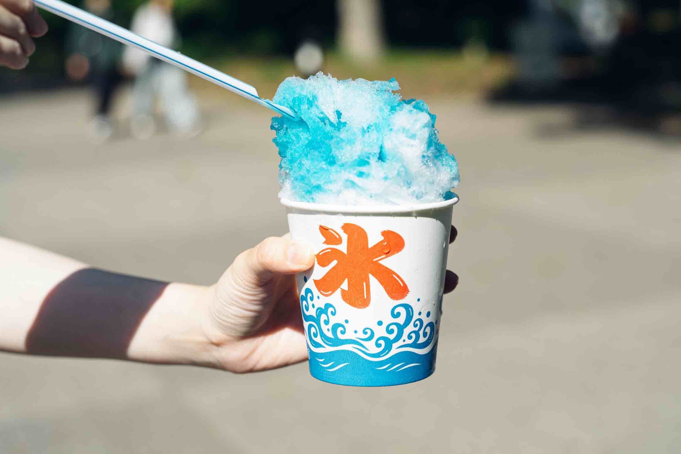 A hand holding a paper cup filled with blue kakigōri, Japanese-style shaved ice.