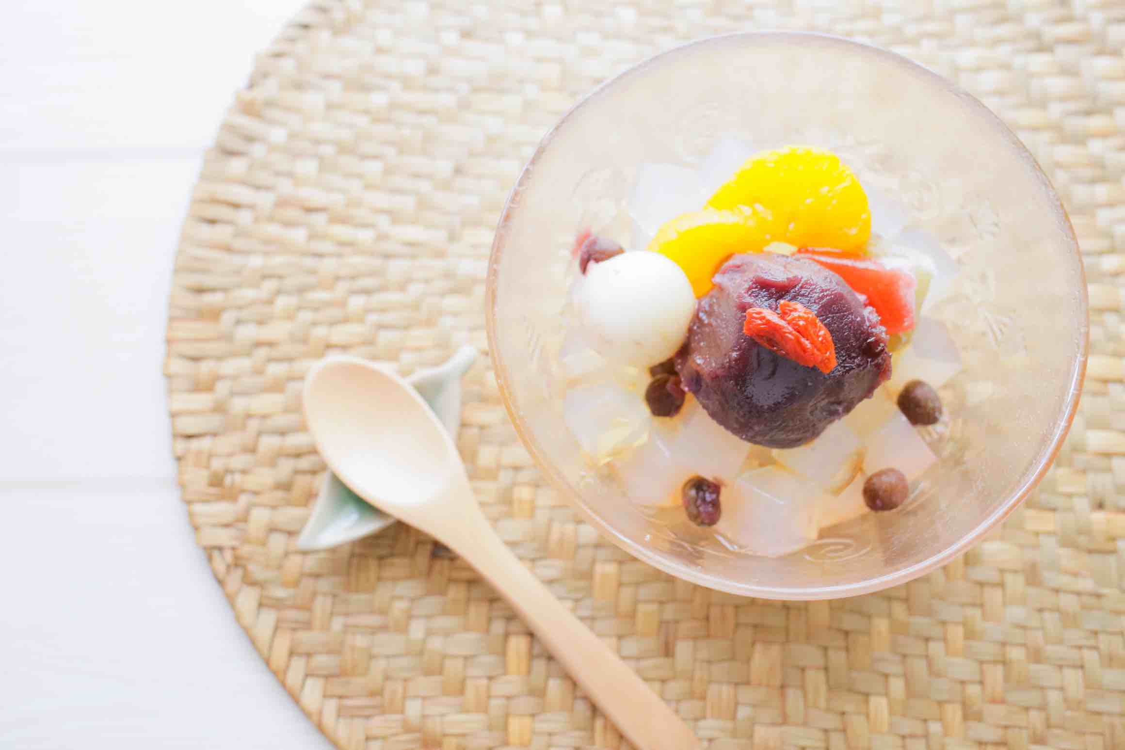 A glass bowl of anmitsu: a traditional Japanese dessert with agar jelly, red bean paste, mochi, and fruits.