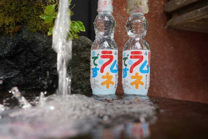 Two bottles of Ramune soda cooled in a stream of running water.