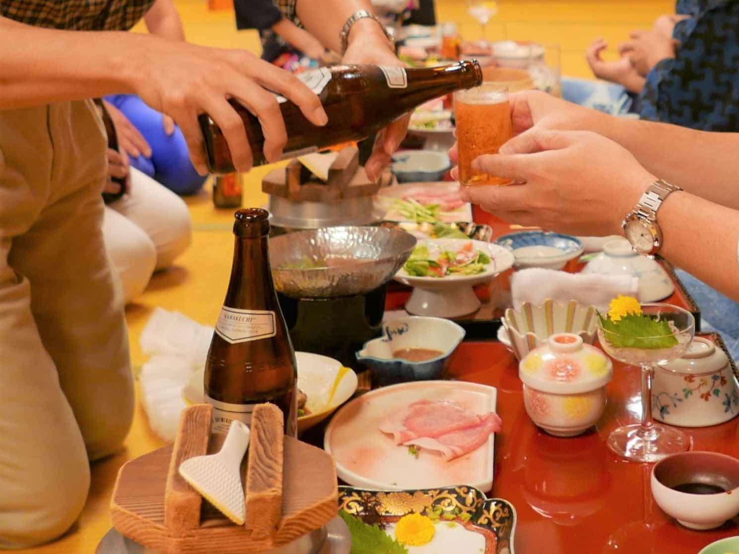 People pouring and receiving beer at a traditional Japanese banquet with assorted dishes.