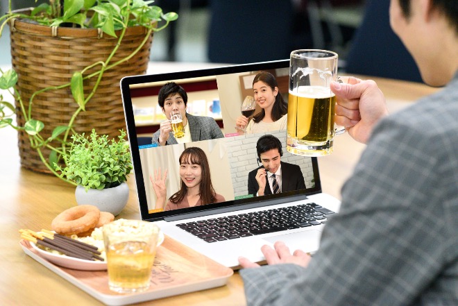 Person holding a beer while joining a virtual nomikai with colleagues on a laptop screen.