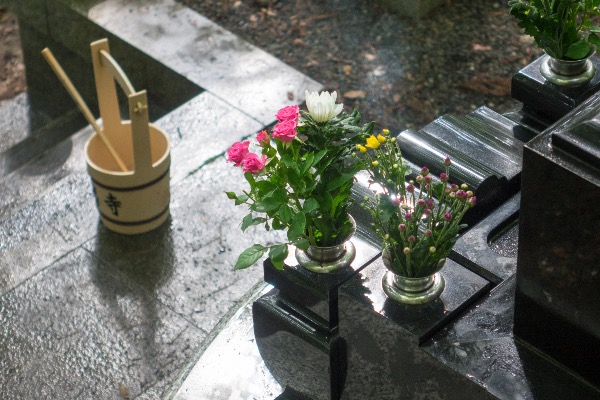 Fresh flowers placed on a gravestone during an Obon ohakamairi visit, with a water bucket and ladle nearby.