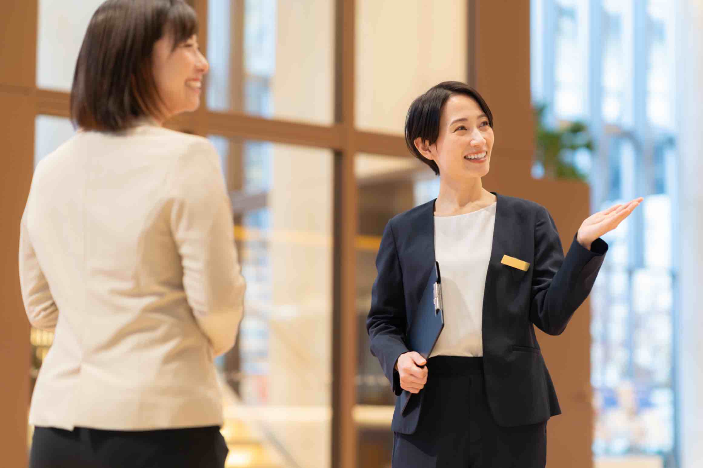 Smiling hospitality staff member in a suit welcoming and assisting a guest in a bright lobby.