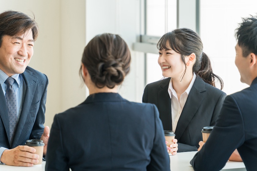 Group of Japanese colleagues chatting and smiling over coffee.