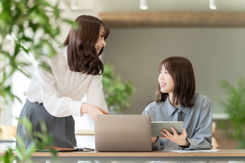 Two colleagues collaborating with a laptop and tablet in an office.
