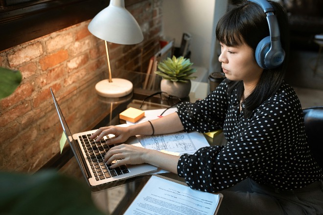 Intern working with focus on her laptop, wearing headphones at a tidy desk.