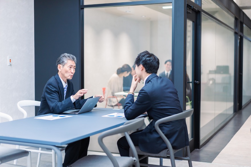 A mentor and intern in a business meeting discussing work across a table.