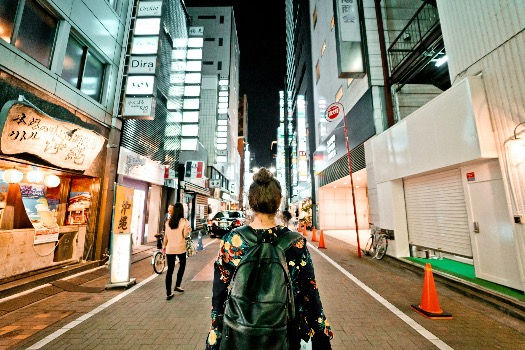 A young woman with a backpack walking through Tokyo’s lively streets at night.