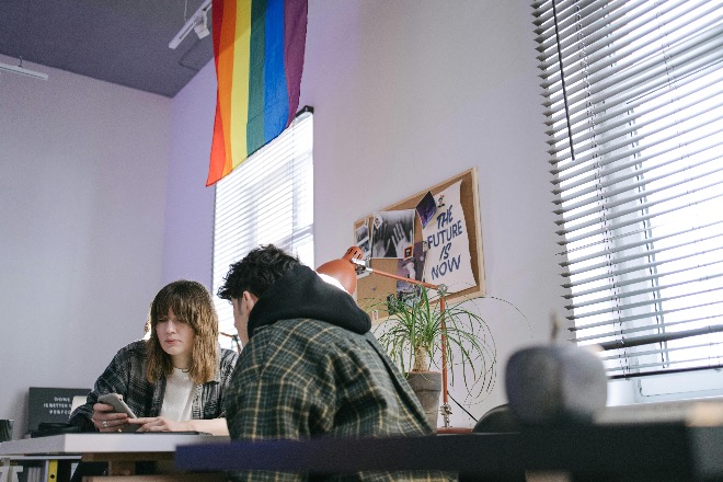 Two young professionals working together in an office decorated with a pride flag