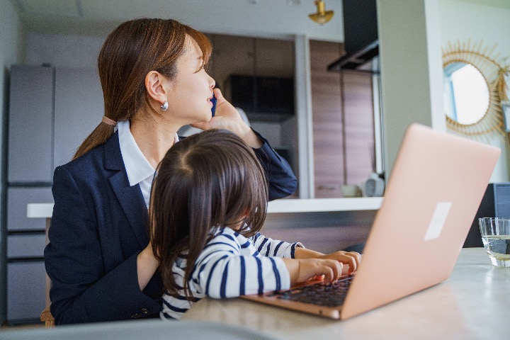 Japanese working mother speaking on the phone while holding her child and using a laptop at home.