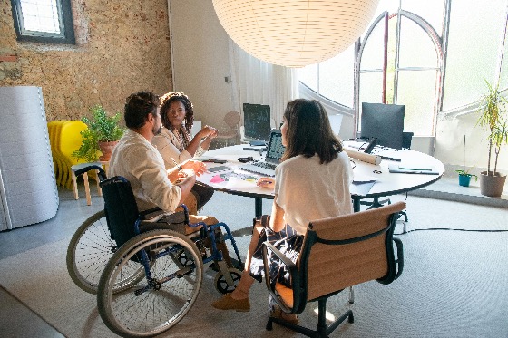 Diverse team collaborating in an office, including a professional in a wheelchair, representing inclusivity and teamwork.