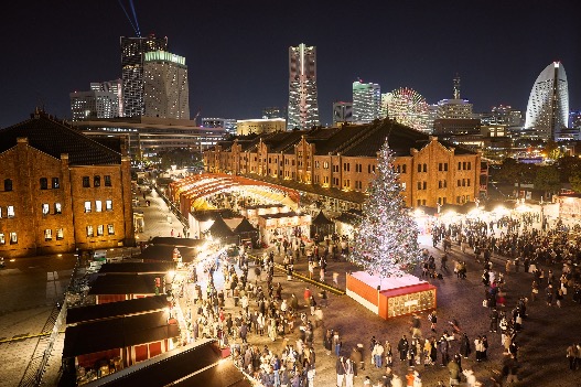 Crowds walking through the Yokohama Red Brick Warehouse Christmas Market at night with illuminated stalls and a large Christmas tree.