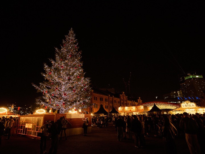 Illuminated Christmas tree and market stalls at night during a holiday event in Japan.