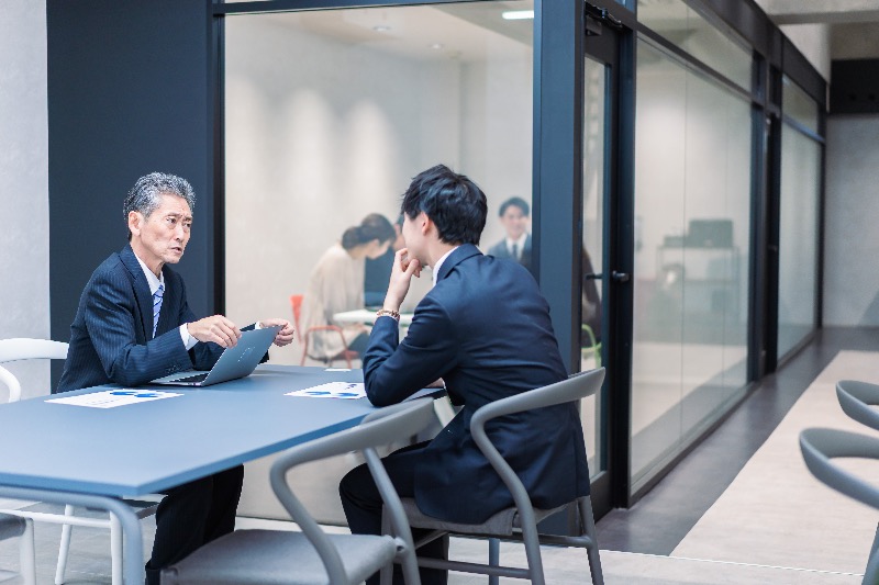 A senior manager conducting a formal performance review with an employee inside a modern Japanese office.
