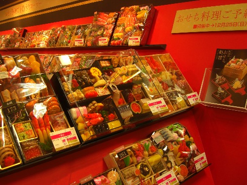 Image shows plastic replica models of osechi ryōri sets displayed for reservation at a Japanese department store ahead of the New Year.