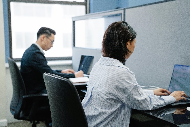 Japanese office workers seated at desks using computers.