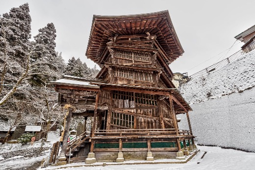 Exterior view of the wooden Sazae-do hall in Aizu, showing its multi-level structure surrounded by snow.