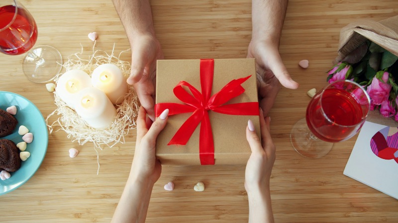 Hands exchanging a wrapped gift box with a red ribbon