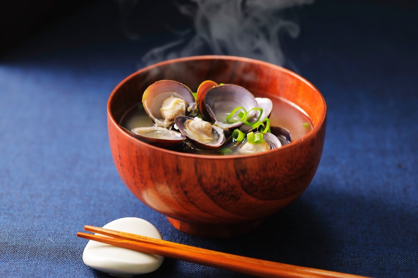 Bowl of hamaguri clam soup served in a lacquer bowl with open clam shells and sliced green onion.