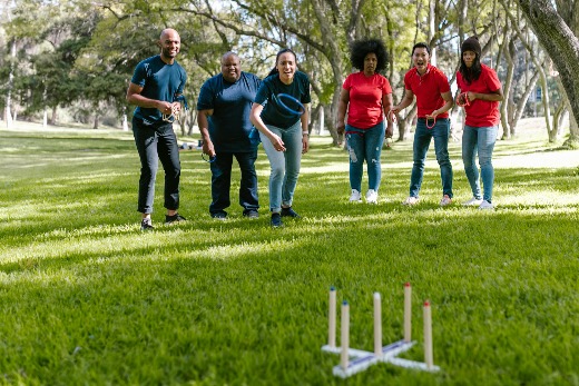 Group of people standing on grass in a park playing a ring toss game as part of an outdoor team activity.