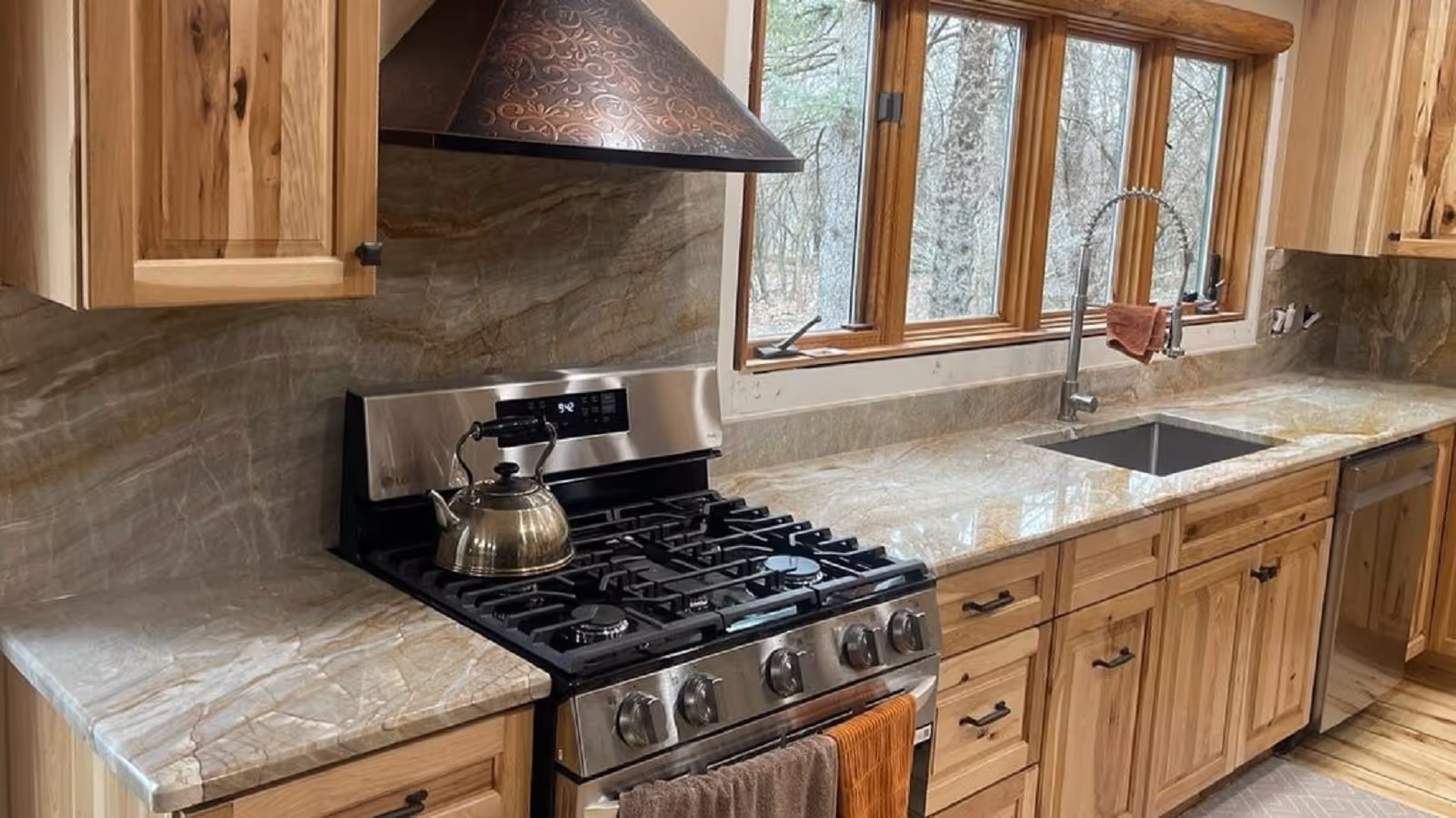 Rustic kitchen featuring Nacarado Quartzite countertops and backsplash, knotty wood cabinetry, and copper range hood.