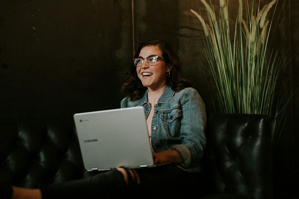 Young girl holding laptop sitting on a couch working on social media posts 